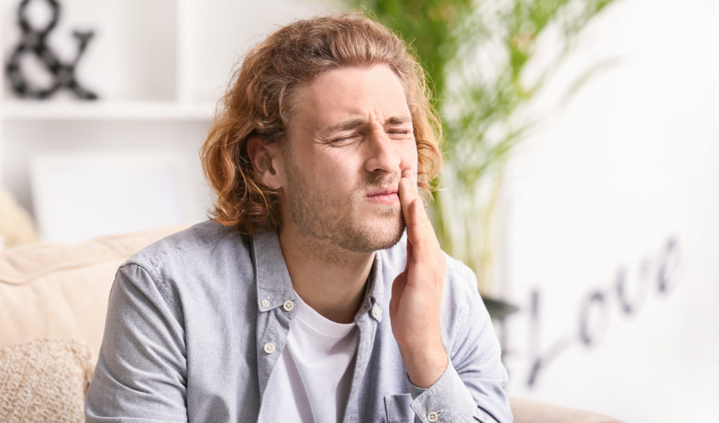 Mann hält sich Wange wegen Zahnschmerzen