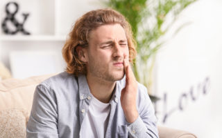 Mann hält sich Wange wegen Zahnschmerzen