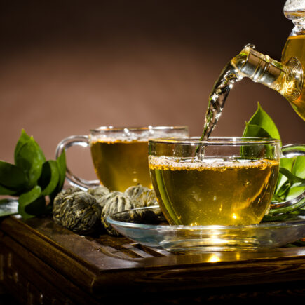 Grüner Tee wird von einer Kanne in eine Tasse gegossen