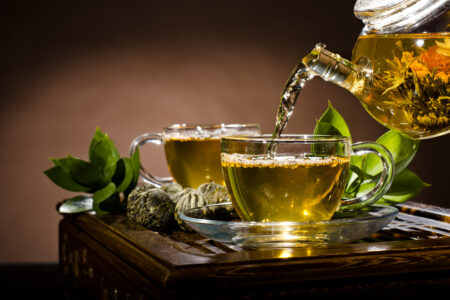 Grüner Tee wird von einer Kanne in eine Tasse gegossen