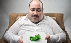 Dicker, trauriger Mann mit einem Teller auf dem wenig Salat liegt