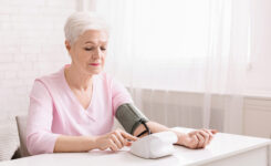 Seniorin sitzt zu Hause am Tisch und misst Blutdruck