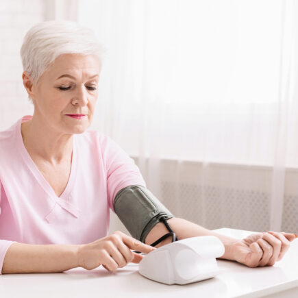 Seniorin sitzt zu Hause am Tisch und misst Blutdruck