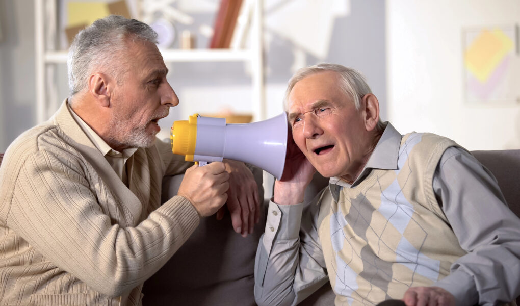 Mann mittleren Alters unterhält sich mit Megafon mit einem alten Mann, der kein Hörgerät hat
