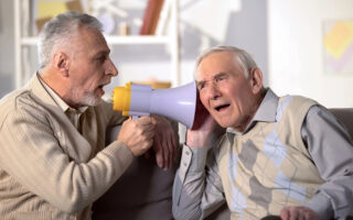 Mann mittleren Alters unterhält sich mit Megafon mit einem alten Mann, der kein Hörgerät hat
