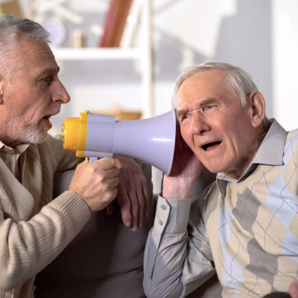Mann mittleren Alters unterhält sich mit Megafon mit einem alten Mann, der kein Hörgerät hat