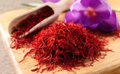 Auf einem hellen Holztisch ist eine Safranblüte, eine Holzschaufel mit Safran Fäden und im Vordergrund befinden sich aufgehäufte Safran Fäden