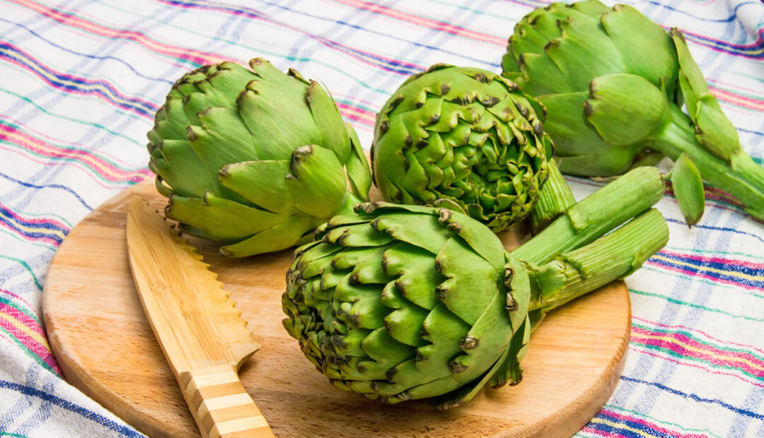 Artischocken auf Holzbrett mit Holzmesser 